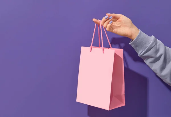 Ženská ruka drží růžový papír nákupní taška na fialovém pozadí. Koncept dodání nákupního prodeje — Stock fotografie