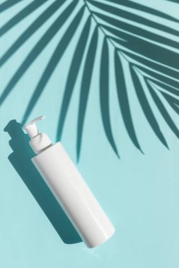 Mavi arka planda palmiye yaprağı gölgesi olan bir şişe krema.