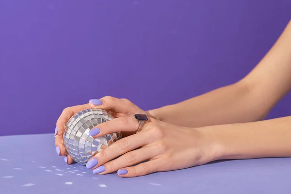 Manikúra ženské ruce drží disco míč na fialovém pozadí. Manikúra, pedikúra salon krásy koncept — Stock fotografie