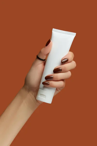 Womans hand holding white tube on brown background. Self care concept. — Stock Photo, Image