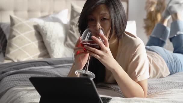 Gelukkig mooie vrouw in casual kleding praten op video oproep op digitale tablet liggend op het bed. Spelen spel winkelen online ontspannen. — Stockvideo