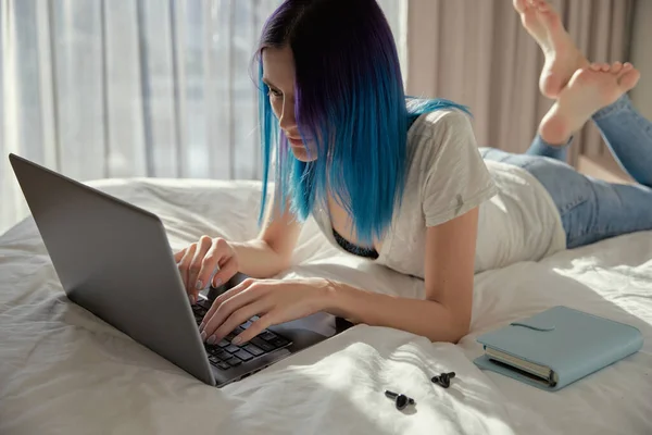 Poważna kobieta z niebieskimi włosami w sypialni praca z laptopem. — Zdjęcie stockowe