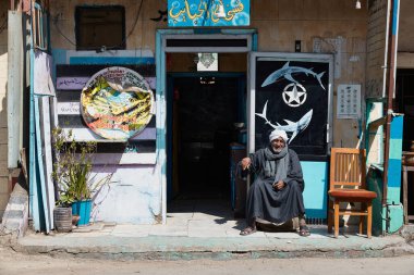 HURGHADA, EGYPT - 19 Şubat 2022: Mağazasının yanında oturan geleneksel giysili yerel bir adam. Otantik gerçek Mısırlı ihtiyarın portresi.