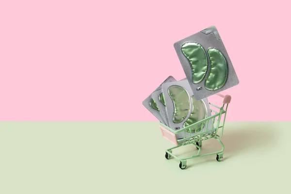 Oční pásky v nákupním vozíku na zeleném zadečku. Péče o obličej krása koncepce — Stock fotografie