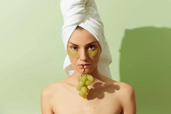 Kvinna med hjälp av grapeseed-baserade ögonlappar på pastell grön bakgrund. Naturlig hållbar hudvård — Stockfoto