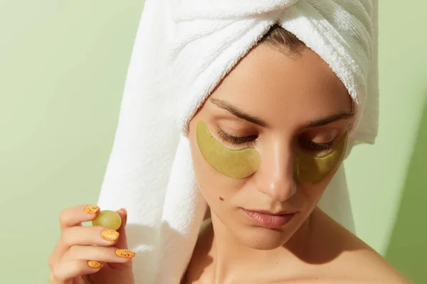 Woman using grapeseed-based eye patches on pastel green background. Natural sustainable skincare — Stock Photo, Image