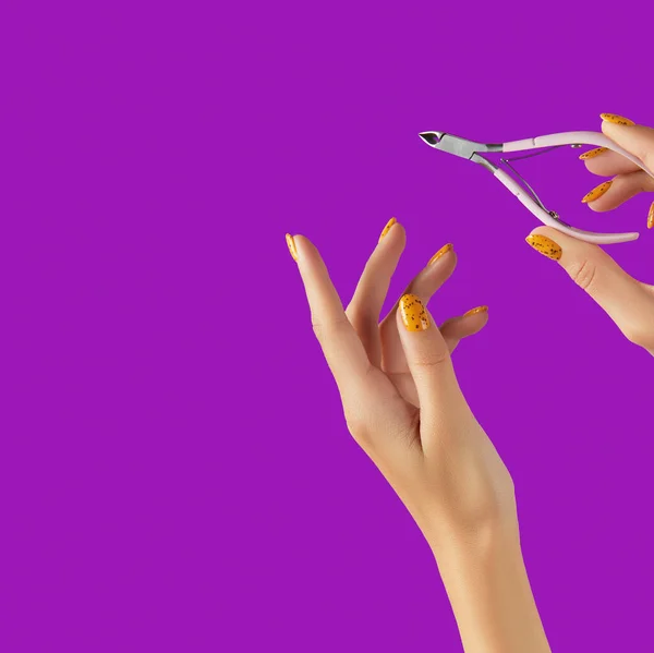 Маникюрные женские руки с модным дизайном ногтей держа ножницы на фиолетовом фоне — стоковое фото