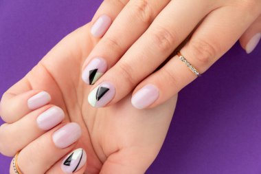 Menekşe arka planında yaratıcı tırnak tasarımı olan kadınların elini kapat