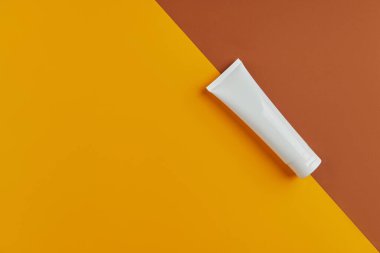 Düz açılı, içi boş, krem ya da turuncu arka planda temizleyici ile dolu beyaz bir tüp vardı. Yüz bakımı konsepti.