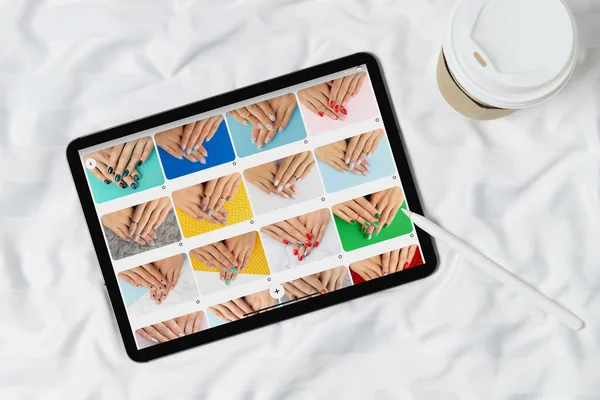 Black tablet with manicure designs on screen on white bed. Beauty salon manicure pedicure concept