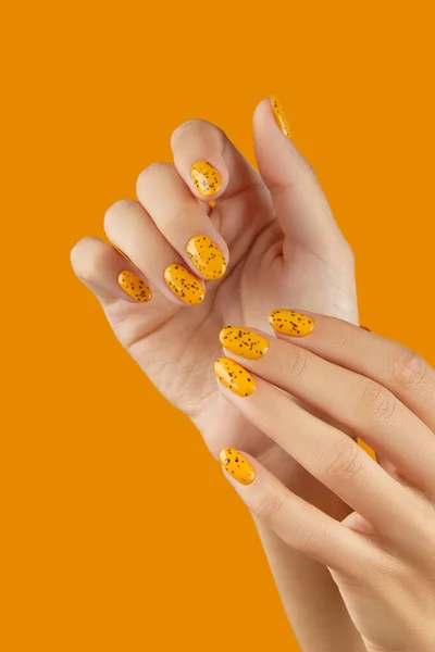 Manicured womans hands with trendy nail design on orange background. Beauty salon concept