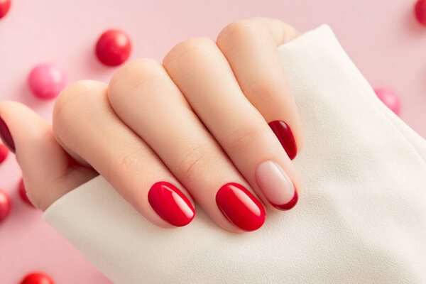 Female hand with manicure on pink background. Christmas Valentines day trendy shiny nail design.