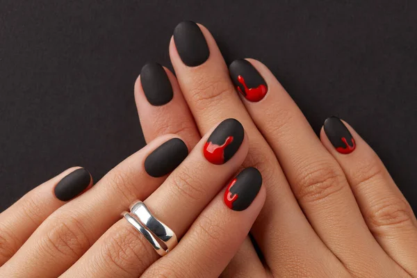 Manicured female hands with fashion accessories on black background. Trendy autumn halloween bloody spooky nail design.