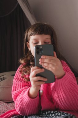 Şirin küçük bebek. Pembe hırkalı, uzun saçlı 5 yaşında kız. Akıllı telefondan büyük bir ilgiyle mesaj atıyor.