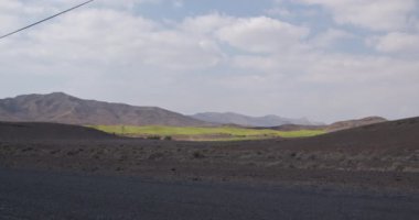 Güzel doğa manzarası. Fuerteventura adasındaki kuru bir çöl bölgesindeki yeşil golf sahası. Büyük dağlar ve arka planda bulutlu bir gökyüzü..