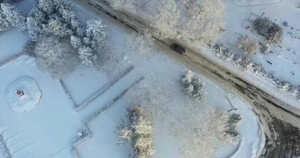 寒い冬の朝に雪に覆われた冬の道を運転する車の空中トップダウンビデオ — ストック動画