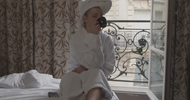 美丽的女人 红头发 身穿白色浴衣 坐在酒店的床上 喝着早晨的咖啡 周末出游的概念 — 图库视频影像