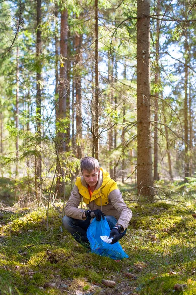 Portrait of a man volunteer collecting garbage to the blue bag in the Estonian forest. The concept of environmental pollution. Spring forest in the background.