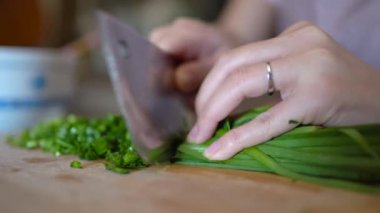 Mutfakta yemek hazırlarken tahta kesme tahtasıyla taze yeşil otlar kesen tanınmamış bir kadın.