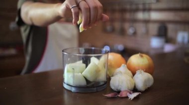 Önlüklü isimsiz kadın aşçı mutfakta tezgahta yemek pişirirken blender 'a sarımsaklı karanfil ekliyor.