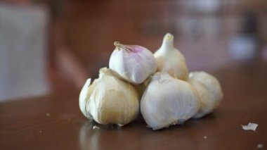 Tanımlanamayan bir kadın, ev mutfağında yemek pişirirken kesme tahtasını kesmek için taze sarımsak alıyor.