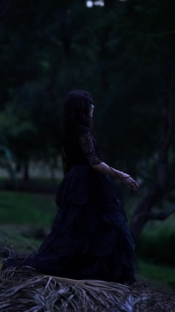 夜に森の中で夢のように踊る長い黒のドレスで優雅な魔女のショットのサイドビュー — ストック動画