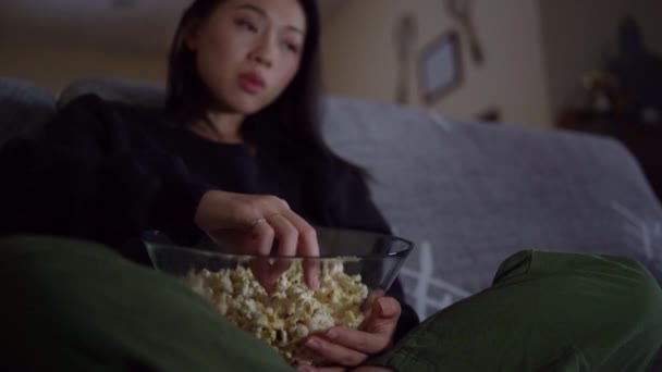 年轻的亚洲女性穿着休闲装 双腿交叉坐在沙发上 在家里吃爆米花 — 图库视频影像
