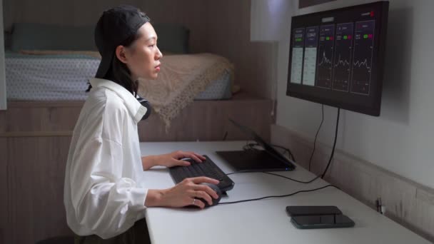 便利な職場での暗号通貨の価値の変化の動的を示すチャートでコンピュータに取り組んでいる集中アジアの女性の側面図 — ストック動画