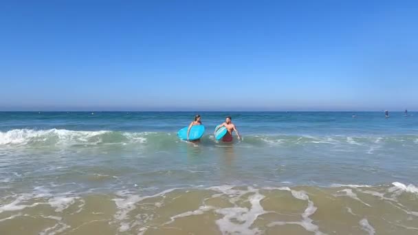 熱帯リゾートの水の上を歩いている間 サーフボードがお互いを見ている水着でスポーツカップルの完全な体 — ストック動画