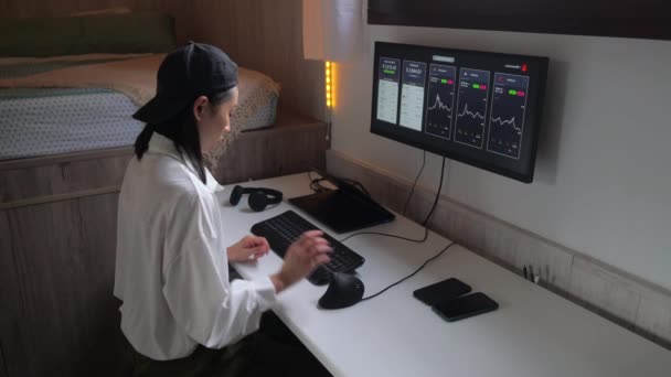 便利な職場での暗号通貨の価値の変化の動的を示すチャートでコンピュータに取り組んでいる集中アジアの女性の側面図 — ストック動画