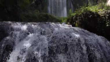 Güneşli bir günde ağaçların altındaki şelaleden