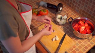 Evdeki mutfakta yemek pişirirken önlüklü, sarımsak doğrayan bir kadının yan görünüşü