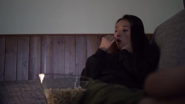 若いですアジアの女性身に着けていますカジュアル服上のソファと食べるポップコーンで家 — ストック動画