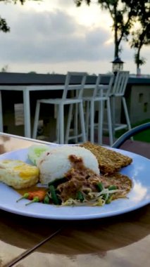 Nasi Pecel, güneşli tarafı yukarıda yumurta ve Tempe, öğleden sonra beyaz tabakta servis ediliyor.