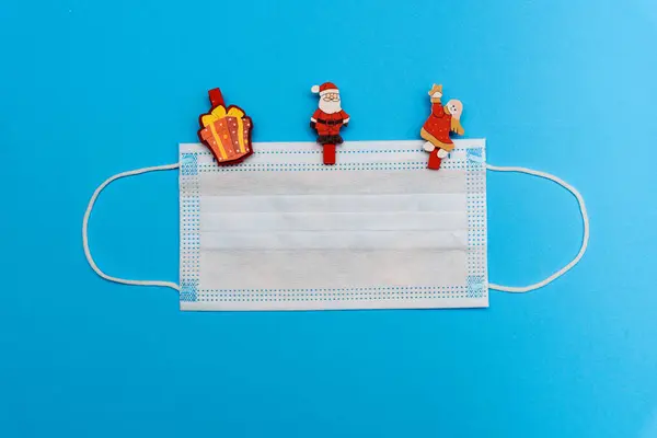 Mavi arka planda bir tıbbi maske, içinde çipler, hediye şeklinde oyuncaklar, Noel Baba ve bir melek. Kopyalama alanı olan üst görünüm, metin için boşluk. Yeni yılı kutluyoruz. Mutlu yıllar 2022 konsepti..