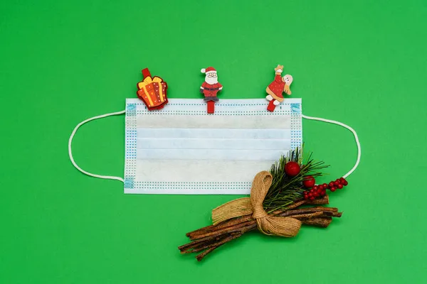 Yeşil arka planda bir tıbbi maske, ladin dalları ve broşlarla Noel Baba ve melek şeklinde oyuncaklar. Kopyalama alanı olan üst görünüm, metin için boşluk. Mutlu yıllar 2022 konsepti..