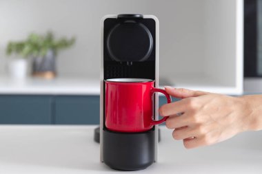 Kapsül kahve makinesi ve kırmızı fincanda espresso. Modern, rahat mutfakta taze kahve yapılıyor. Kahvaltı zamanı.