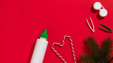 Gözlük düzeltme personeli Noel hediyesi kartı: kontakt lensler, cımbız ve kontak lens solüsyonu kırmızı arka planda Noel ağacı dalı ve şeker kamışı ile. Yüksek kalite fotoğraf