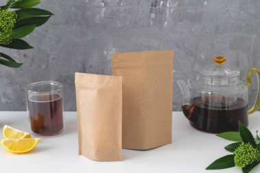 Çay için kahverengi karton paketler, çay fincanı, limon ve gri arka planda çaydanlık. Çay markası ve ambalaj modeli. Yüksek kalite fotoğraf