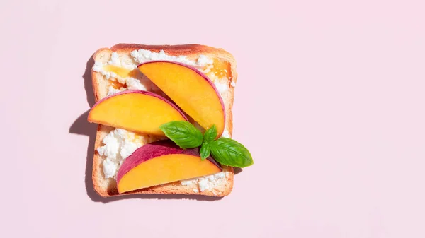 Toasted bread with peach and ricotta cheese on pink background. High quality photo