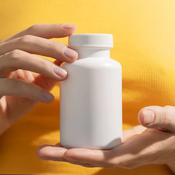 Young female hands holding blank white squeeze bottle plastic tube on yellow background. Packaging for pills, capsules or supplements. Mockup. High quality photo
