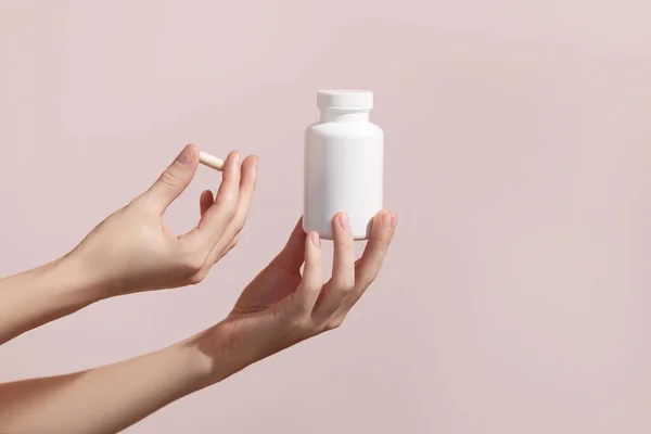 Woman holding pill and blank white plastic tube on pink background. Packaging for pill, capsule or supplement. Medic product branding mockup. High quality photo