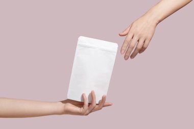 Female hand holds white cardboard packaging for tea/coffee/snack on pink background. Branding and packaging mockup. High quality photo