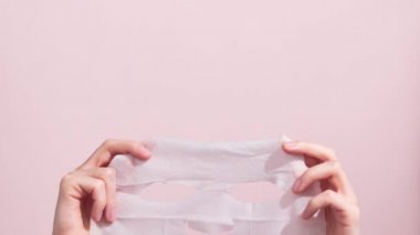 Female hands holding sheet of white mask on pink background. Stop motion animation.