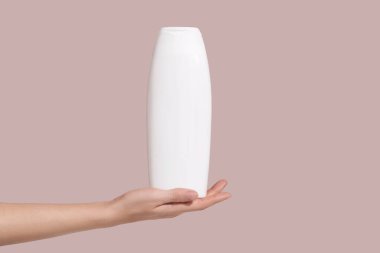 Hand holding blank white plastic tube on pink background. Cosmetic beauty product branding mockup. Copy space. High quality photo