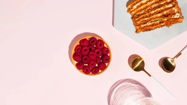 Raspberry tart and piece of honey cake on pink background. High quality photo