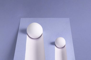 İki beyaz top yokuş aşağı yuvarlanıyor ve mor bir arka planda iz bırakıyor..