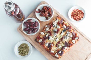 mozzarella, keçi peyniri, kurutulmuş domates ve siyah zeytinli küçük kare pizza.