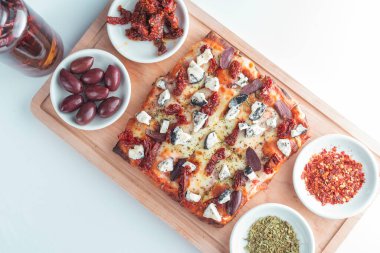 mozzarella, keçi peyniri, kurutulmuş domates ve siyah zeytinli küçük kare pizza.