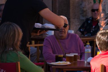 ALBARRACIN, İSPAIN, 11 Ekim 2021: Sabahın keyfini çıkaran turistlerle dışarıda servis yapan bir garsonun ayrıntıları. Paket servis. Açık hava barının terasında öğle yemeği.
